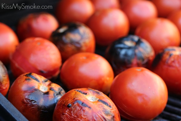 Horizontal image of lots of tomatoes on the grill being charred to make fire roasted tomatoes. 