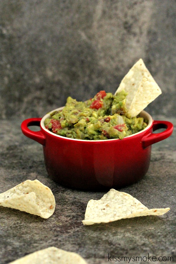 Grilled Guacamole served in a red dish with nacho chips scattered around.