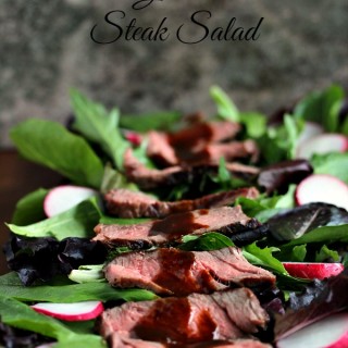 Grilled steak salad loaded with greens, radish and steak, all covered in a drizzle of balsamic sauce. Plate in on a dark counter with a dark background.