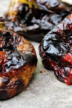 Fire Roasted Bell Peppers charred to perfection and sitting on a light grey surface while cooling down.
