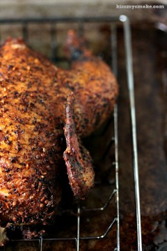 Smoked whole chicken cooked to perfection and resting on a metal cooling rack on a dark counter.