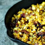 Charred skillet corn with bacon in a black cast iron pan on a tile counter.