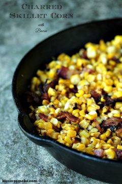 Charred skillet corn with bacon in a black cast iron pan on a tile counter.