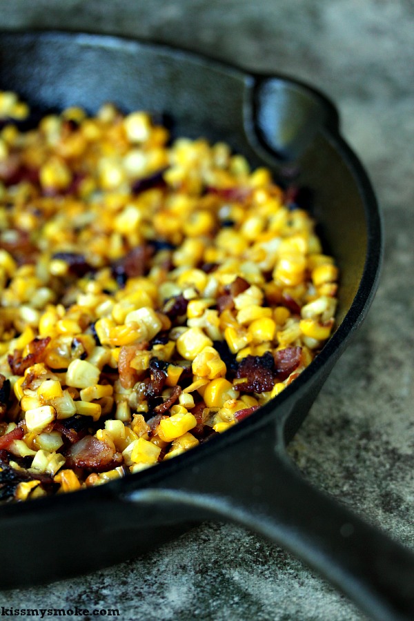 Close up image of Charred skillet corn with bacon in a black cast iron pan on a tile counter.