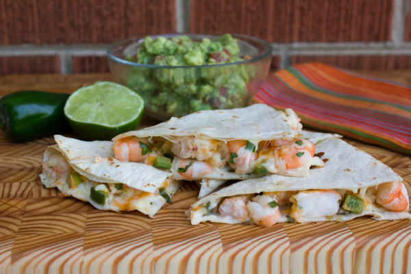 Shrimp and Jalapeno Quesadilla stacked on a wood board with garnish in the background.