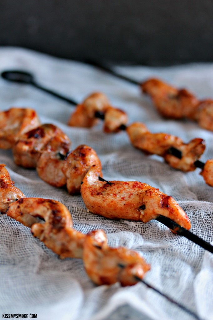 Grilled chicken skewers cooked to perfection on black metal skewers and sitting on a white surface.