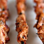 Grilled chicken skewers cooked to perfection on black metal skewers and sitting on a white surface.