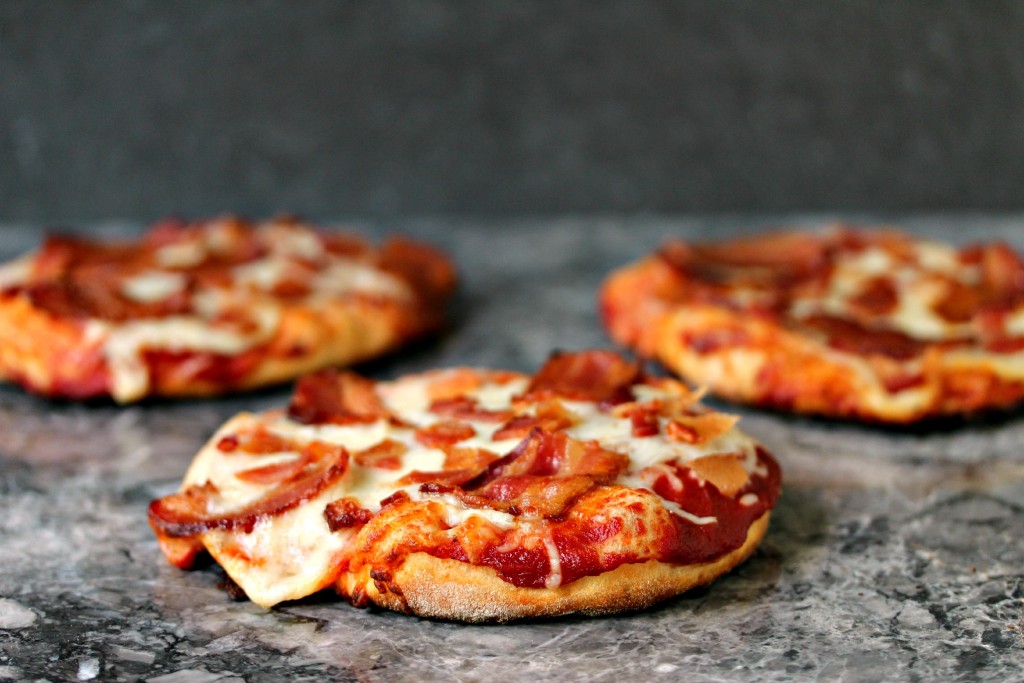Grilled mini pizzas topped with cheese and bacon. Three mini pizzas are sitting on a grey counter.