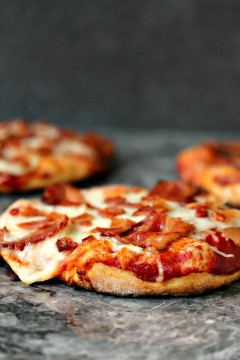 3 mini grilled pizzas topped with cheese and bacon on a grey counter.