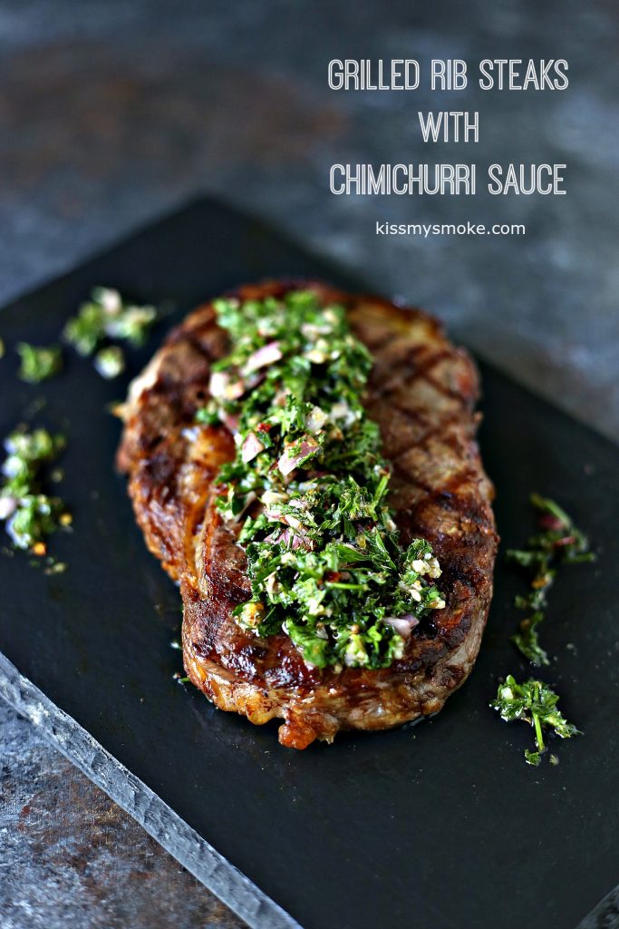 Grilled Rib Steaks cooked to perfection and smothered with Homemade Chimichurri Sauce! Steak is sitting on a black serving tray that is sitting on a dark counter. Text in upper right corner of image states recipe and blog name. 