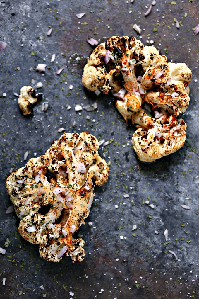 overhead image of grilled spicy cauliflower steaks on a dark surface
